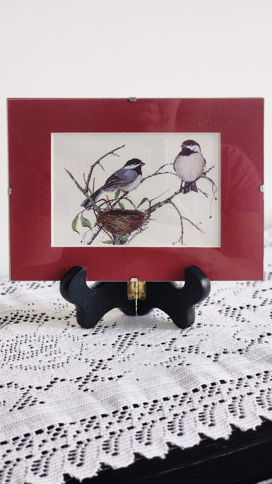 Framed Black-Capped Chickadee print by Vermont artist Nancy Revoir Dezotell in cranberry red frame on easel