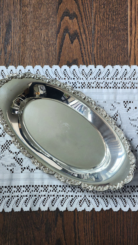 Oval Oneida silverplate bread tray with an ornate rose-and-scroll border on a lace runner